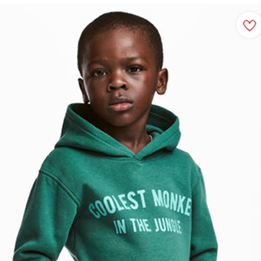 A young boy wearing a green hoodie with the text Coolest Monkey in the Jungle printed on the front, standing against a plain white background.